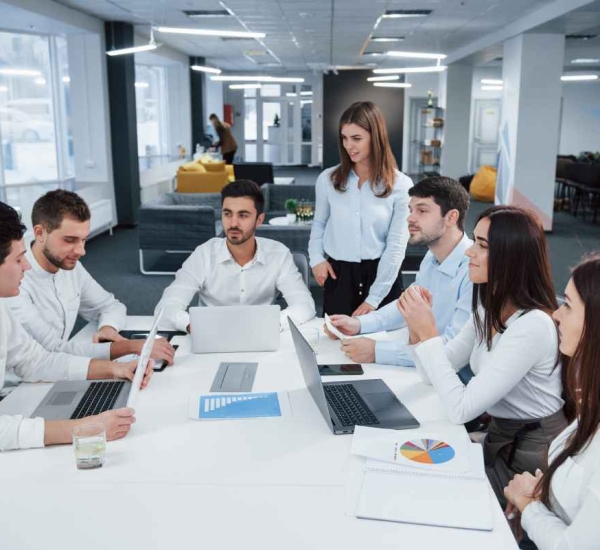 Guy on the left side talking and colleagues is listening to him. Group of young freelancers in the office have conversation and smiling.